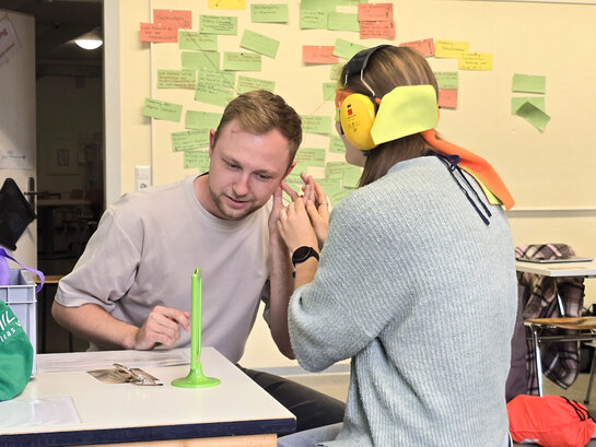 Das Foto zeigt Studierende in einem Seminarraum, die lernen, wie bei Taubblindheit kommuniziert wird. Sie tragen dafür Kopfhörer und eine Augenbinde.