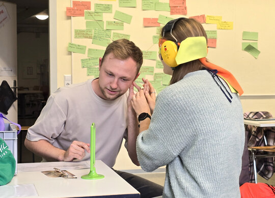 Das Foto zeigt Studierende in einem Seminarraum, die lernen, wie bei Taubblindheit kommuniziert wird. Sie tragen dafür Kopfhörer und eine Augenbinde.