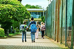 mehrere Grundschulkinder mit ihren Ranzen von hinten 