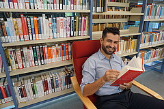 Das Bild zeigt einen Mann, der auf einem Sessel im Lesesaal der Pädagogischen Hochschule Heidelberg ein Buch liest.