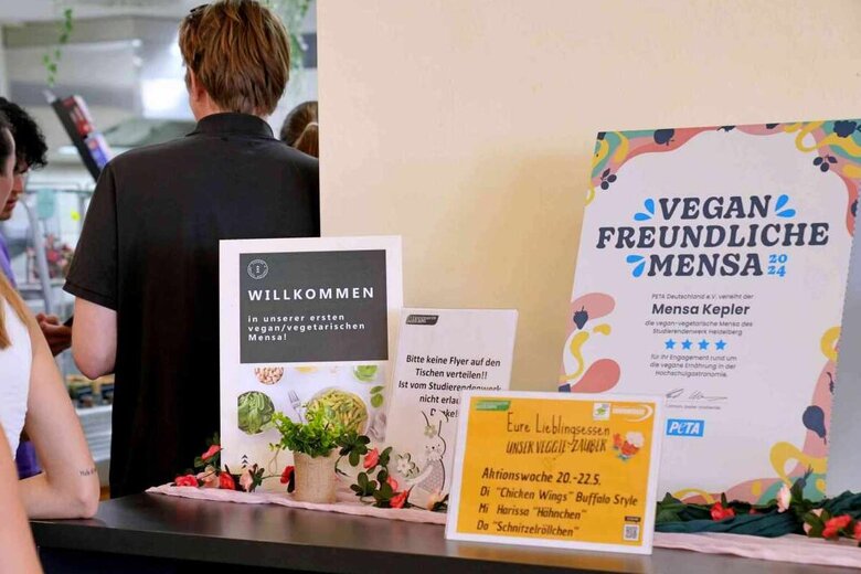 Zu sehen sind Studierende in der Altbau-Mensa der PH Heidelberg. Auf einem Tisch in der rechten Bildhälfte befindet sich ein Zertifikat der PETA Stiftung.