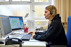 Das Foto zeigt eine Person mit Headset vor zwei Monitoren an einem Tischarbeitsplatz.