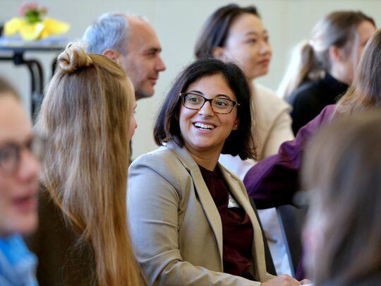 Blick ins Publikum der DGFF-Tagung, wobei der Fokus auf einer jungen Wissenschaftlerin liegt, die eine andere Teilnehmerin anstrahlt. Das Bild wurde in der Aula der PHHD aufgenommen. 