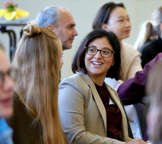Blick ins Publikum der DGFF-Tagung, wobei der Fokus auf einer jungen Wissenschaftlerin liegt, die eine andere Teilnehmerin anstrahlt. Das Bild wurde in der Aula der PHHD aufgenommen. 