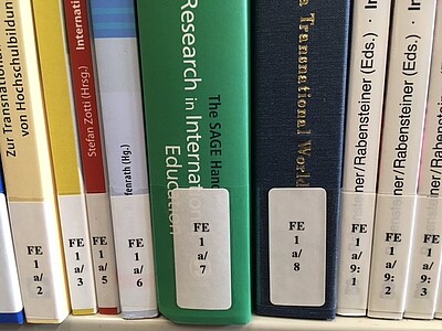 The photo shows the spines of books standing next to each other with the shelfmark FE 1a on the topic of "Internationalisation of Teacher Education".