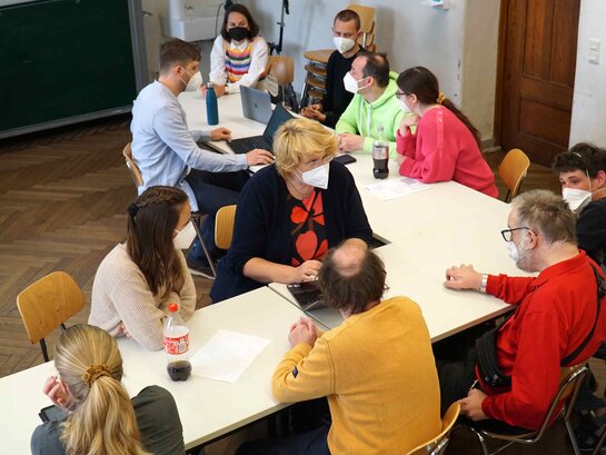 Das Bild zeigt eine Gruppe von Menschen, die an einem langen Tisch sitzen und ins Gespräch vertieft sind.