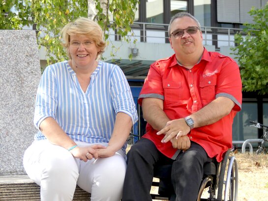 Das Bild zeigt Karin Terfloth und Helmuth Pflantzer. Beide sitzen vor dem Neubau der Pädagogischen Hochschule Heidelberg und läheln in die Kamera.