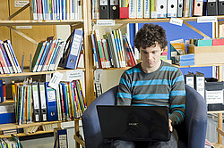 Student am Laptop in der Bibliothek.