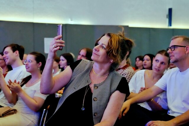 Zu sehen ist eine Dame im Publikum, die ein Foto mit ihrem Handy aufnimmt.