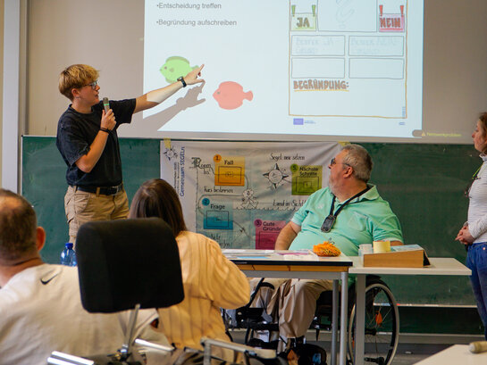 Das Foto zeigt verschiedene Personen in einem Seminar sitzen.