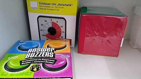 Weitere Materialien, die sich im Unterricht einsetzen lassen, darunter vier Buzzer, eine Zeitdauer-Uhr und ein bunter Würfel, auf dessen Seiten sich Steckfächer aus Folie befinden. So lässt er sich individuell auf den Unterricht anpassen.