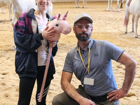 Trainer Sebastian und Athletin Hanna auf dem Reitplatz - im Hintergrund Einhörner.