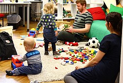 Das Bild zeigt zwei Eltern die mit ihren zwei Kindern auf dem Boden spielen.