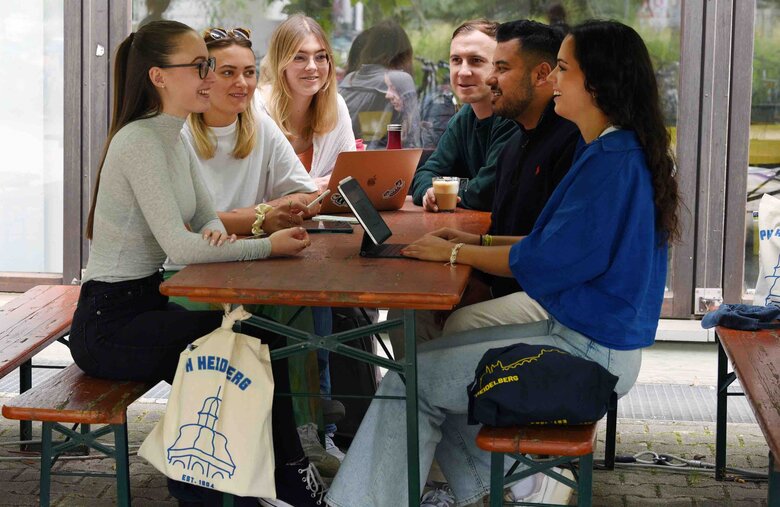 Studierende sitzen an einem Tisch im Außenbereich der Pädagogischen Hochschule Heidelberg. Symbolbild der Fachschaft Biologie.