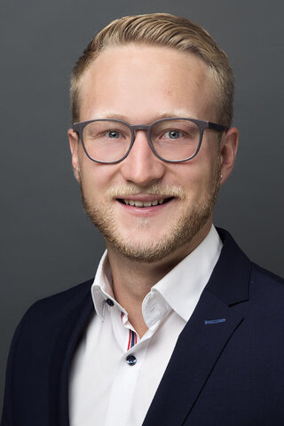 Zu sehen ist ein Portraitfoto von Dr. Valentin Unger vor schwarz-dunkelgrauem Hintergrund.