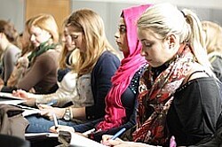 Das Symbolbild zeigt eine Reihe von Studierenden von der Seite. Sie schreiben bzw. hören zu. Eine trägt ein pink farbenes Kopftuch. Copyright Pädagogische Hochschule Heidelberg