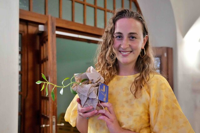 Zu sehen ist eine Alumna mit einer Pflanze, welche alle Absovlent:innen sich als Erinnerung mitnehmen konnten.