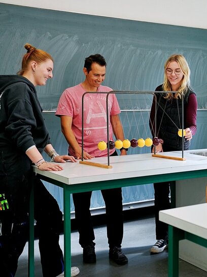 Studierende der Physik stehen vor einem Newton-Pendel.