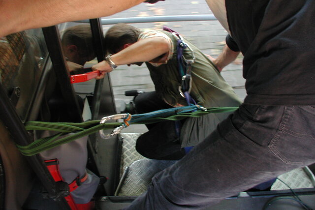 Ein Kameramann lehnt sich aus der offenen Tür eines fahrenden Linienbusses und filmt dabei.