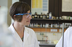 Frau mit weißem Kittel und Schutzbrille.