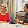 Frauke Janz schaut lächelnd direkt in die Kamera. Wolfgang Schultz schaut sie an und spricht deutlich mit den Händen-