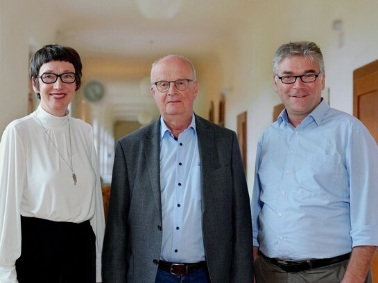 Das Foto zeigt drei Personen in die Kamera lächeln.