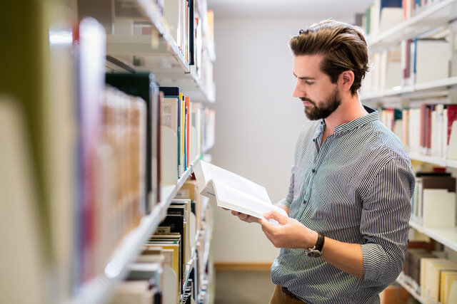 Zu sehen ist ein Student in einer Bibliothek. 