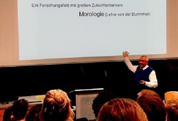 Auf dem Bild sieht man Prof. Joachim Funke etwas an einer Leinwand im Hörsaal erklären.