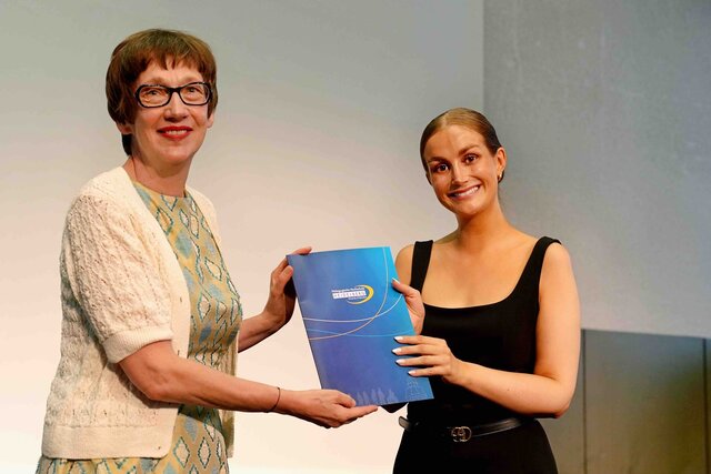 Zu sehen ist Rektorin Vach, wie sie einer Alumna den Bestehensbrief in einer PHHD-Mappe überreicht.