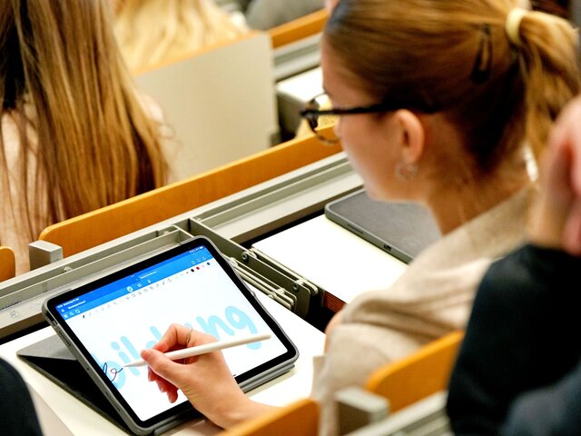 Eine Studentin sitzt im Hörsaal der Pädagogischen Hochschule Heidelberg. Sie schreibt "Bildung" auf ihrem Tabletbildschirm.