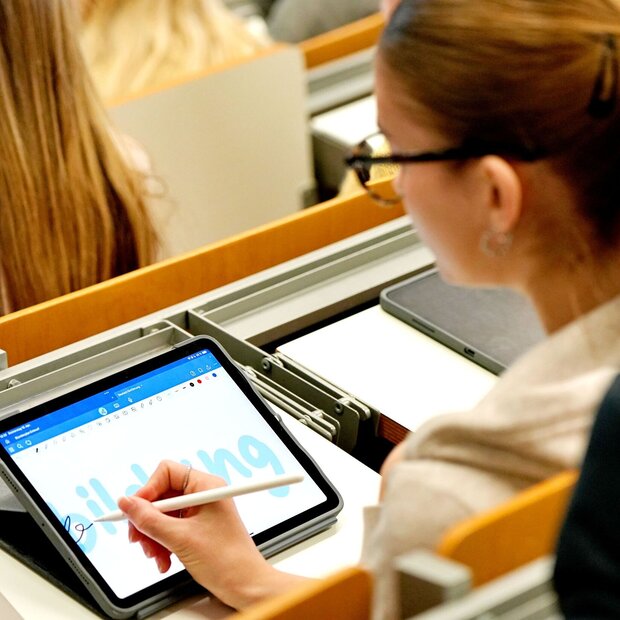 Eine Studentin sitzt im Hörsaal der Pädagogischen Hochschule Heidelberg. Sie schreibt "Bildung" auf ihrem Tabletbildschirm.