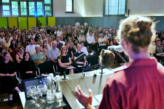 Zu sehen ist Absolvent Oskar Müller von hinten sowie das Publikum, während seiner Ansprache "Was ist die PHHD für mich?"