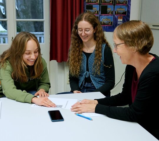 Zu sehen sind die Hilfskräfte Marlene Endrolath und Laura Klüven im Gespräch mit Antje Karbe aus der Kommunikation.