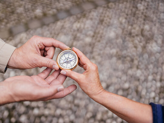 Drei Hände halten einen Kompass.