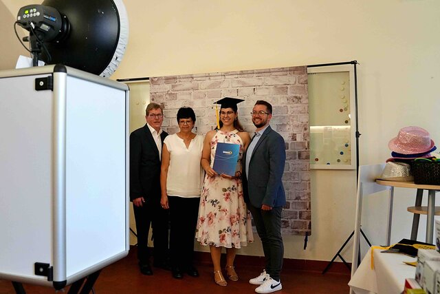 Zu sehen ist eine Alumna mit Graduierungshut und PHHD-Mappe sowie Freund und Eltern bei der Benutzung der Fotobox.