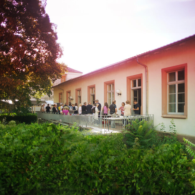 Das Bild zeigt viele Menschen im Gespräch auf der HSE-Terrasse im Abendrot, umgeben von Baum und Büschen.