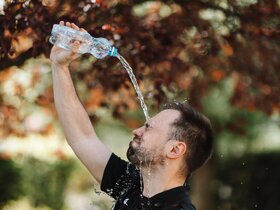 Mann in T-Shirt steht im Freien und gießt sich eine Flasche Wasser über den Kopf