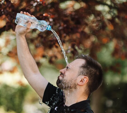 Mann in T-Shirt steht im Freien und gießt sich eine Flasche Wasser über den Kopf