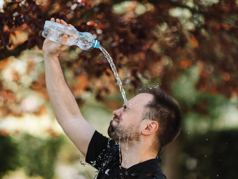 Mann in T-Shirt steht im Freien und gießt sich eine Flasche Wasser über den Kopf