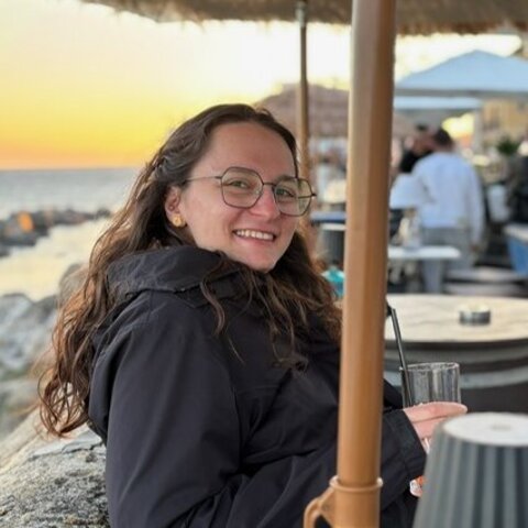Afra mit Glas in der Hand und Strandbar im Hintergrund
