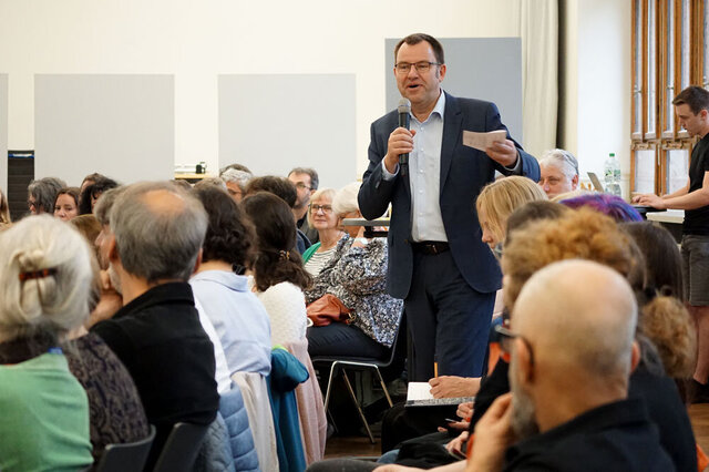 Der Moderator der HRK geht mit dem Mikrofon durch die vollbesetzte Aula der Pädagogischen Hochschule Heidelberg.