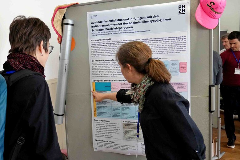 Auf dem Bild sind zwei Personen vor einem Plakat zu sehen.