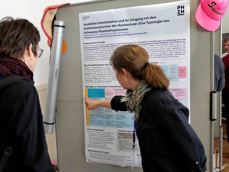 Auf dem Bild sind zwei Personen vor einem Plakat zu sehen.