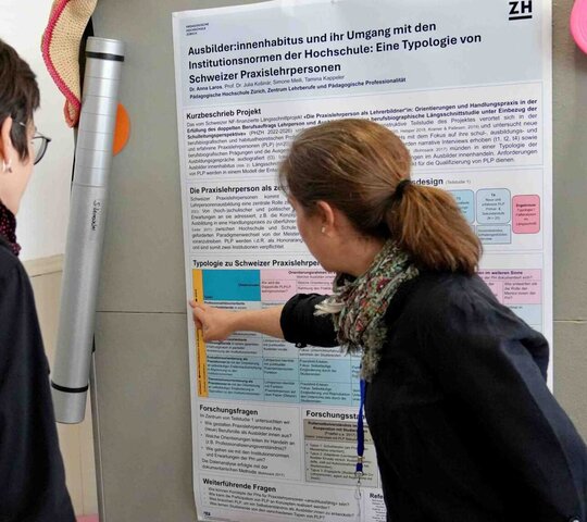 Auf dem Bild sind zwei Personen vor einem Plakat zu sehen.
