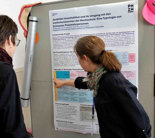 Auf dem Bild sind zwei Personen vor einem Plakat zu sehen.