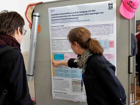Auf dem Bild sind zwei Personen vor einem Plakat zu sehen.