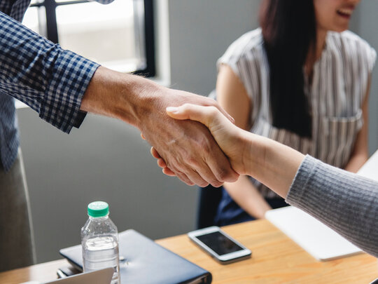 Das Symbildbild zeigt den Arm von zwei Menschen. Sie geben sich die Hand.