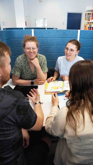 Studierende des Studiengangs für Lehramt Grundschule sitzen zusammen und arbeiten in einer Workbay der Bibliothekt.