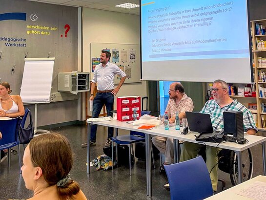 Das Foto zeigt verschiedene Personen in einem Seminarraum interagieren.