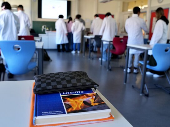 Das Foto zeigt eine Klasse beim Chemieunterricht, im Vordergrund ist ein Chemiebuch zu sehen
